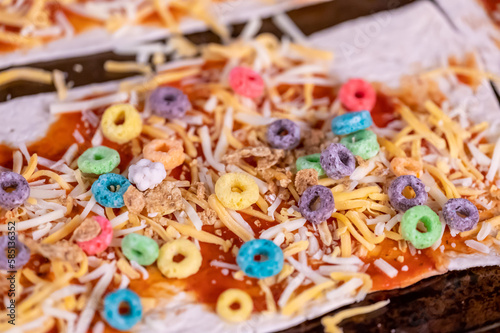 Pizza made by a child with cereal, cheese, and sauce.