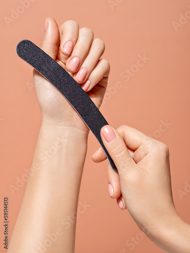 Self treatment in one photo. A closeup of nail care and nail-treatment procedure at home. Beautiful female hands with minimal gel nail polish, holding a nail file creating self-made hygiene manicure