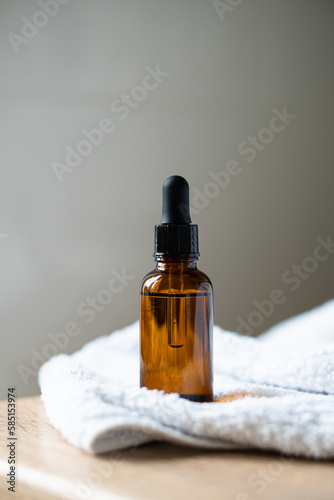 Amber glass serum oil dropper bottle and white towel on table mock-up, cosmetic container daylight shot