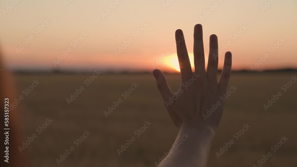 Happy girl stretches her hand to sunset. Sun between fingers of girls hands. Teenager with long hair holds out her hand at sunset. Childhood dream, express emotions in nature. Symbol of kind, warmth