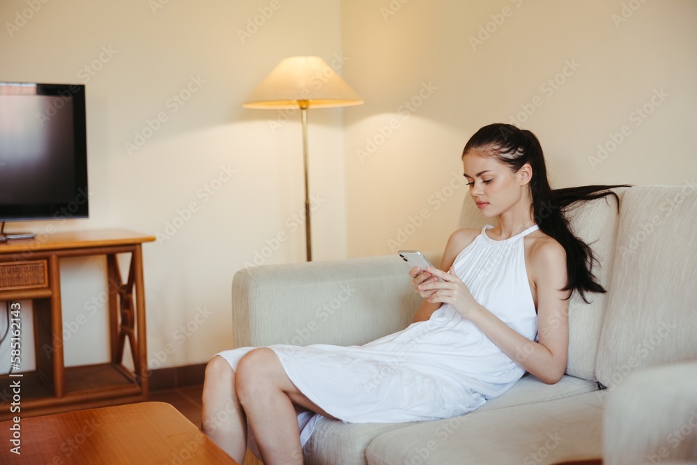 A young woman sits on the couch in the living room with her phone in her hands, relaxing online work and social media freelance blogger. A young woman sits on the couch in the living room with her phone in her hands, relaxing online work and social media freelance blogger.
