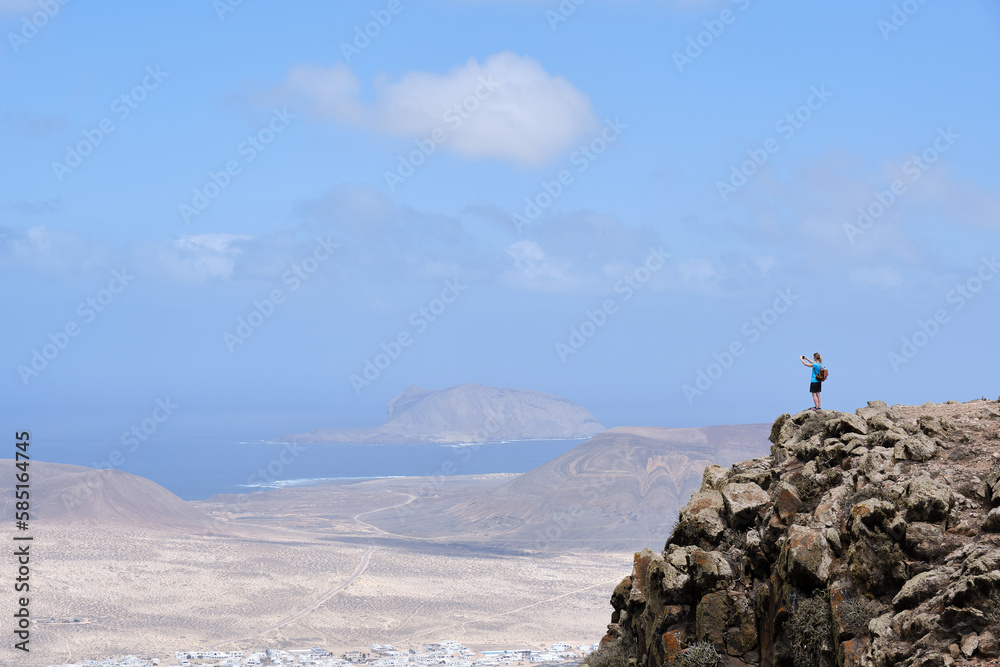 Woman photographing the landscape from a hill. La Graciosa Island in the background.