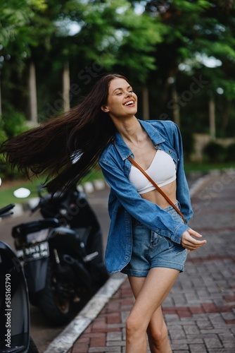 Portrait of woman brunette smile with teeth running down the street against backdrop palm trees in the tropics, summer vacations and outdoor recreation, the carefree lifestyle of a freelance student. © SHOTPRIME STUDIO
