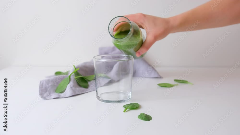 Fresh prepared green spinach smoothie is poured from a carafe into a glass Fresh prepared green spinach smoothie is poured from a carafe into a glass