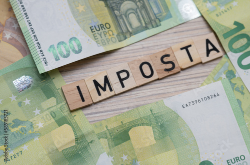 inscription Imposta which means tax in Italian next to euro banknotes. Concept showing the Italian economy