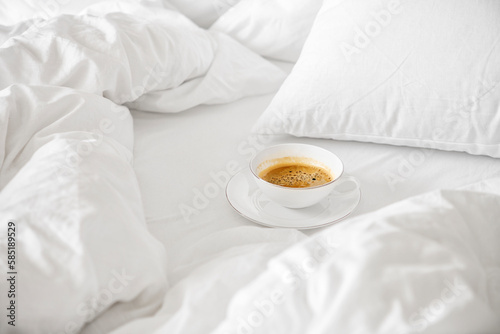 White cup of americano coffee stand on bed with white sheet, blanket and pillows