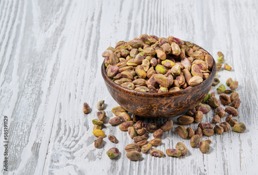 Nuts peeled pistachios in a wooden cup on a white wooden background. Rustic style. The concept of vegetarian and diet snacks. Nuts peeled pistachios in a wooden cup on a white wooden background. Rustic style. The concept of vegetarian and diet snacks.