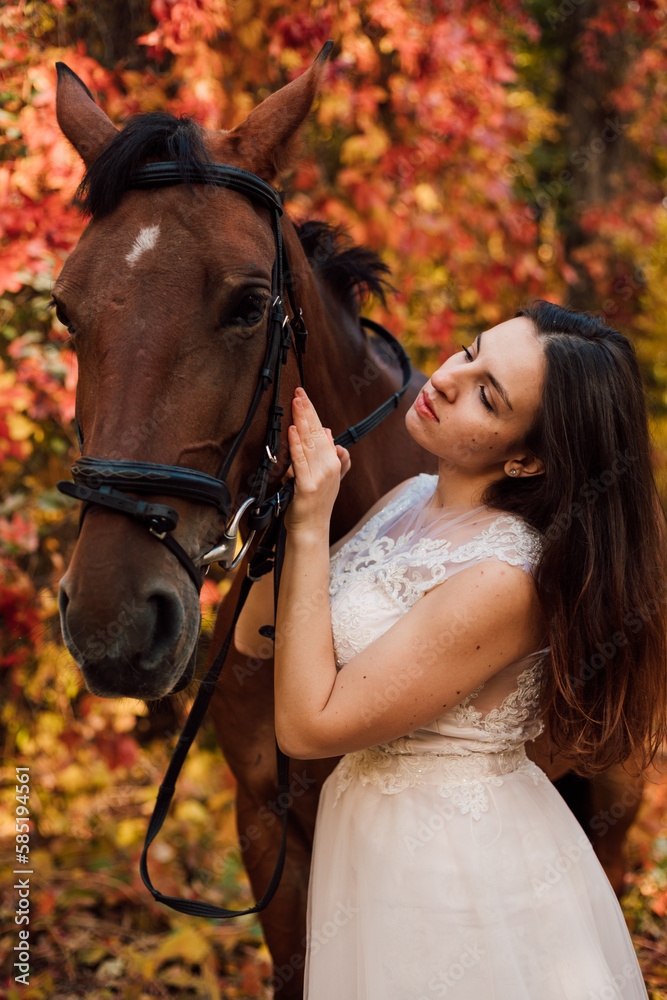 Obraz premium Bride in white dress near a horse in the autumn forest