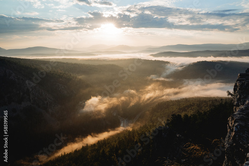 Fog creeps into the river valley early summer morning, sunrise in the mountains, rock cliff, sun glare, golden hour in photography, nature morning © Aleksey