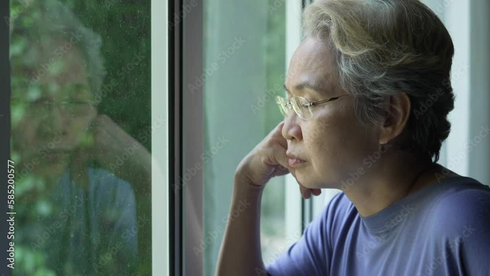 Mature Asian woman with Mental Health issue looking through window.