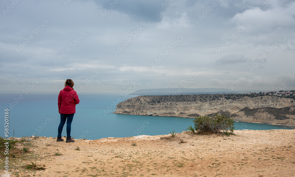 Unrecognized tourist woman standing at the edge of the hill sightseeing enjoying the scenery of a rocky coast