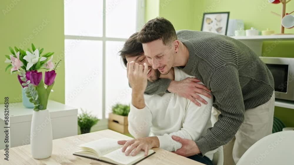 Two men sitting on table kissing at dinning room Two men sitting on table kissing at dinning room
