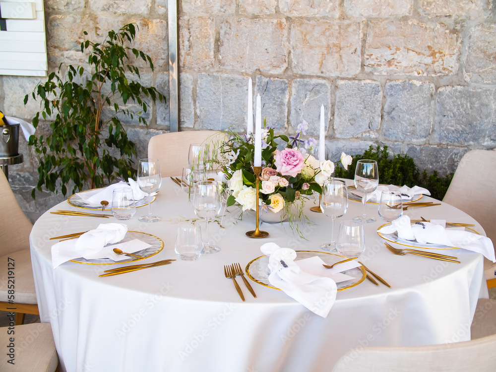 Wedding banquet concept. Chairs and round table for guests, served with cutler and, flowers and crockery and covered with a tablecloth Wedding banquet concept. Chairs and round table for guests, served with cutler and, flowers and crockery and covered with a tablecloth