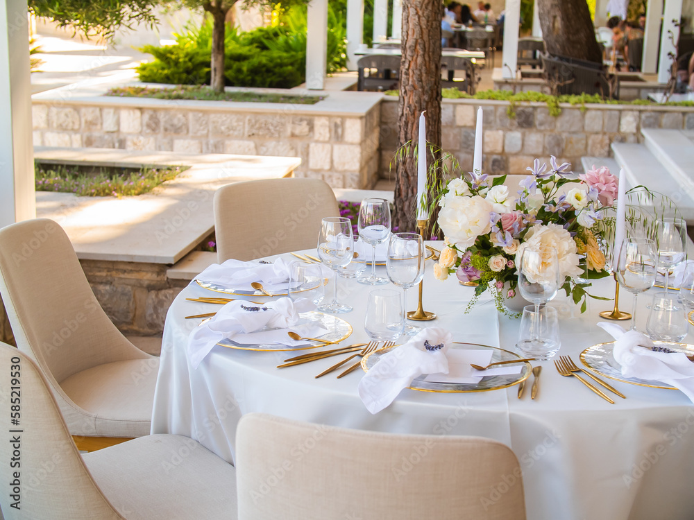 Wedding banquet concept. Chairs and round table for guests, served with cutler and, flowers and crockery and covered with a tablecloth