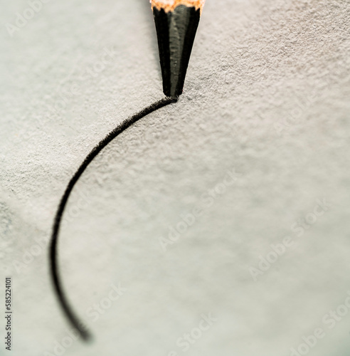 A macro image of a pencil drawing a curved line on a light colored sheet of paper.