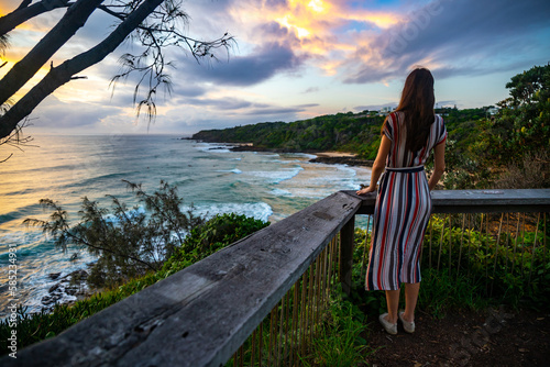 A girl in dress walks along the boardwalk and enjoys the view of the stunning first and second bay Coolum and big waves on Pacific Ocean. Stunning panorama of Sunshine Coast, Queensland, Australia photo