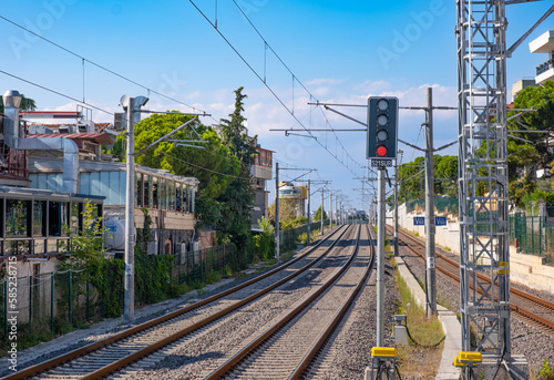Railway tracks in the city on blue sky background. Train station, traffic light shows red signal on railway, stop light