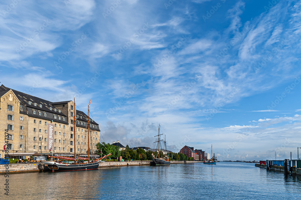 Copenhagen, Denmark - September 13, 2010: Wide panorama with beige stone Admiral Hotel building along Larsens Place and behind Kvaesthusbroen quay with historic sailing yachts under blue cloudscape
