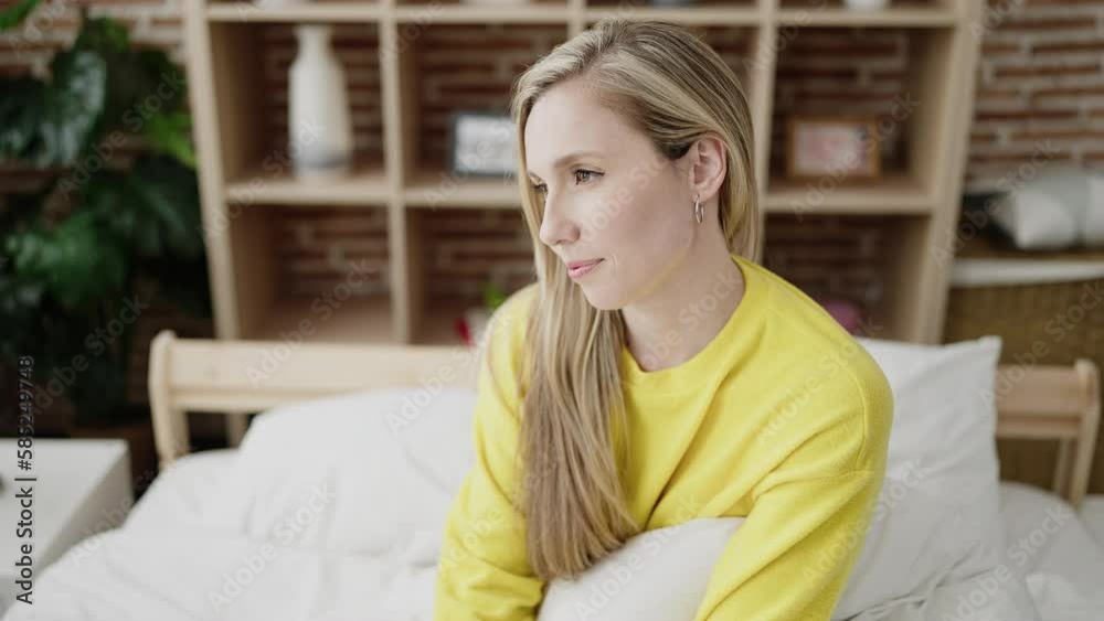 Young blonde woman sitting on bed looking to the side at bedroom Young blonde woman sitting on bed looking to the side at bedroom