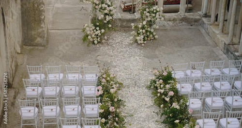 Flower path among decorated white chairs in house inner yard
