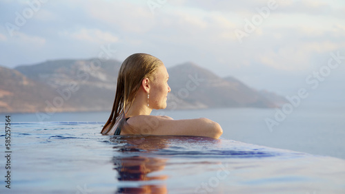 young woman at midday in infinity pool on edge of abyss. girl looks into distance, concept of loneliness and happiness to be alone for peace and tranquility.