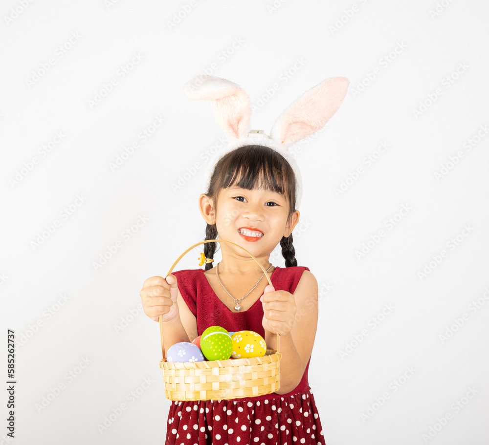 Happy Easter Day. Smile Asian little girl wearing easter bunny ears holding basket of full colorful eggs smiles broadly isolated on white background with copy space, Happy child in holiday Happy Easter Day. Smile Asian little girl wearing easter bunny ears holding basket of full colorful eggs smiles broadly isolated on white background with copy space, Happy child in holiday