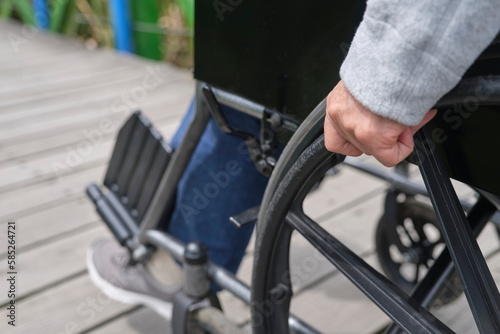 Unrecognizable woman strolling in a wheelchair  outdoors. Close up of a female hand moving the wheelchair forward.