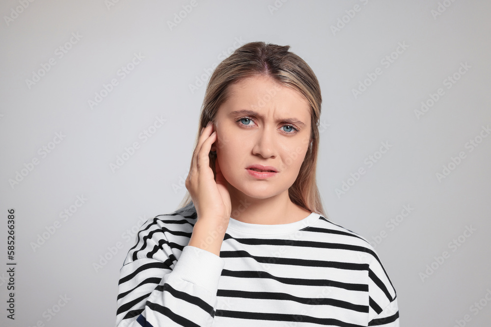 Young woman suffering from ear pain on light grey background Young woman suffering from ear pain on light grey background
