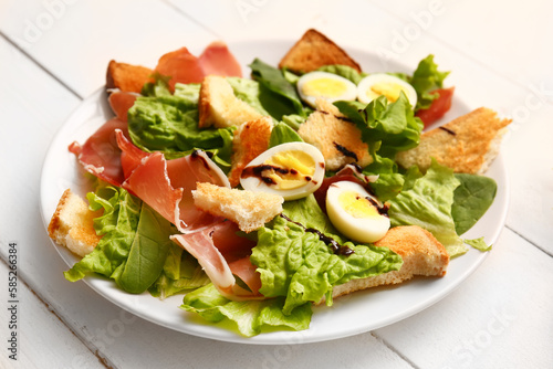 Plate of delicious salad with boiled eggs and jamon on white wooden background