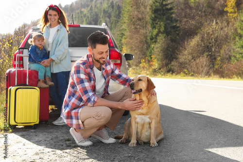 Happy man petting dog, mother and her daughter near car outdoors. Family traveling with pet