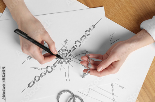 Jeweler drawing sketch of elegant bracelet on paper at wooden table, top view