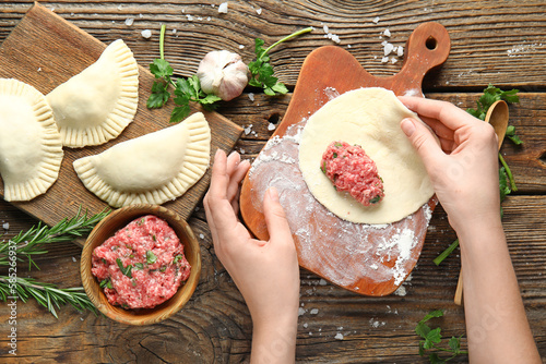 Female hands with raw meat empanadas, forcemeat, herbs and spices on wooden table photo