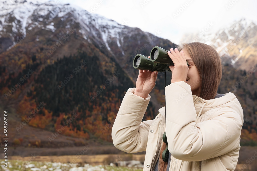 Woman looking through binoculars in beautiful mountains. Space for text Woman looking through binoculars in beautiful mountains. Space for text
