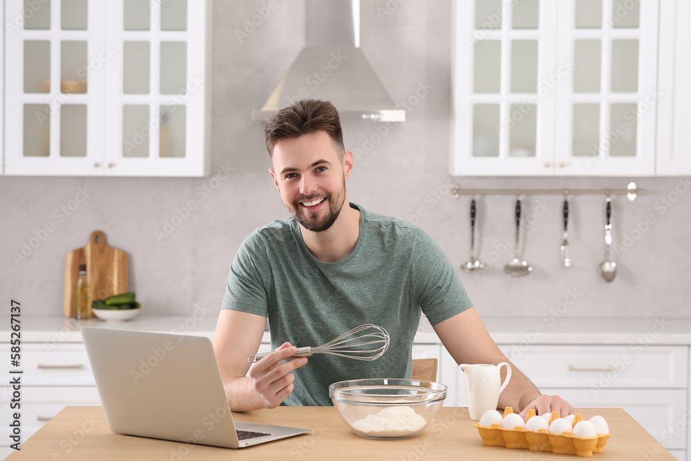 Portrait of man with baking ingredients and laptop at table in kitchen. Time for hobby Portrait of man with baking ingredients and laptop at table in kitchen. Time for hobby