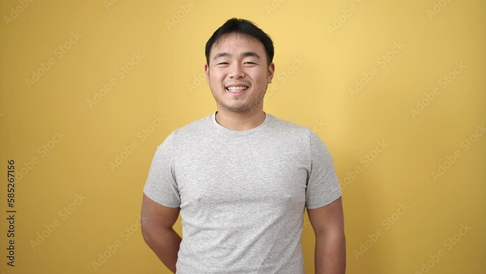 Young chinese man smiling confident standing over isolated yellow background Young chinese man smiling confident standing over isolated yellow background