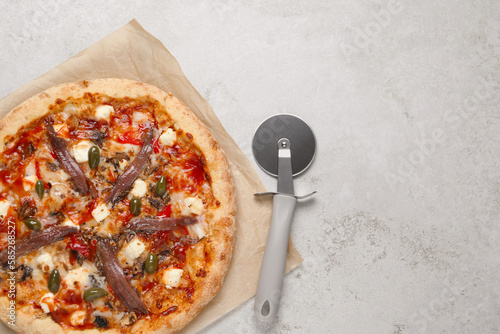Tasty pizza with anchovies and cutter on grey table, top view. Space for text