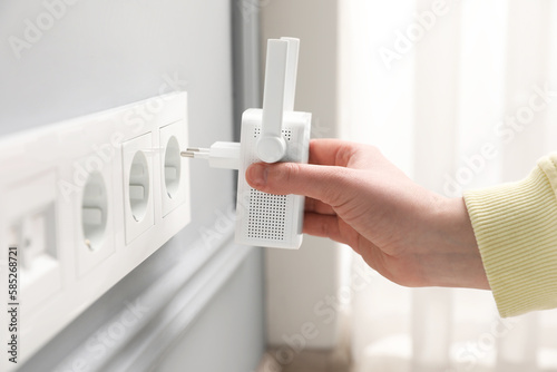 Woman inserting wireless Wi-Fi repeater into power socket indoors, closeup photo