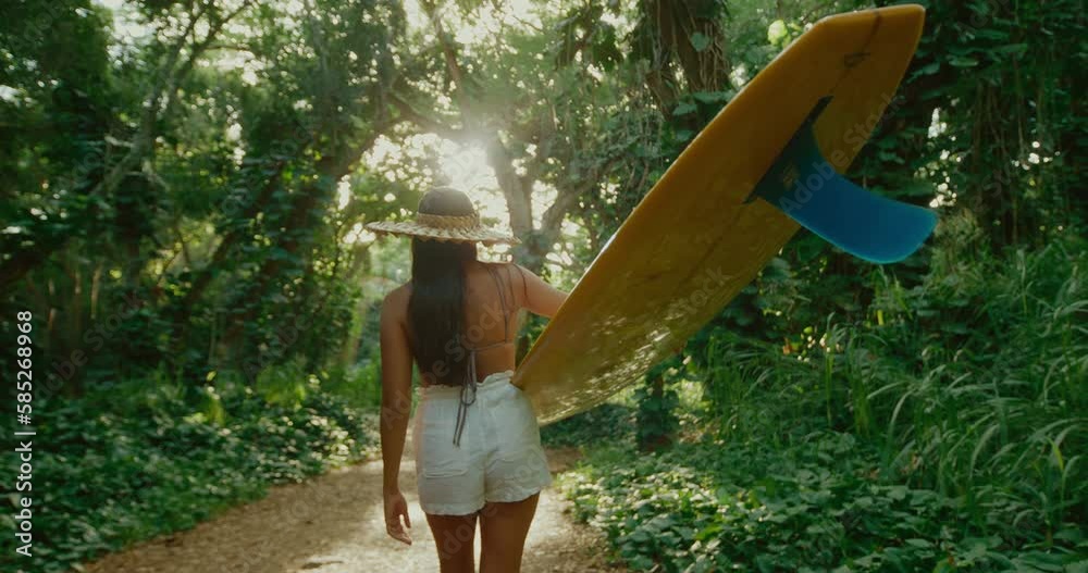 Beautiful Hawaiian surfer girl walking through jungle with classic yellow longboard to go surfing at secret wave, active adventure lifestyle, pacific islander diversity and inclusion
