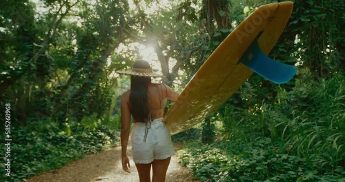 Beautiful Hawaiian surfer girl walking through jungle with classic yellow longboard to go surfing at secret wave, active adventure lifestyle, pacific islander diversity and inclusion