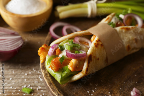 Delicious pita wrap with meat and vegetables on wooden table, closeup