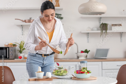 Young woman making vegetable salad in kitchen