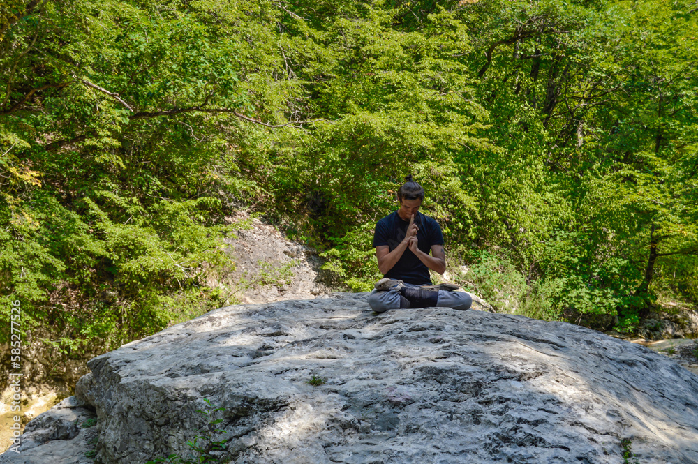This man meditates on a big rock. There is a green forest on the background.