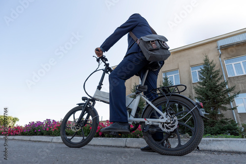 Fototapeta Naklejka Na Ścianę i Meble -  A new modern alternative mode of transport. Eco-friendly electric bike. Hipster businessman commuter with electric bicycle traveling to work in city.
