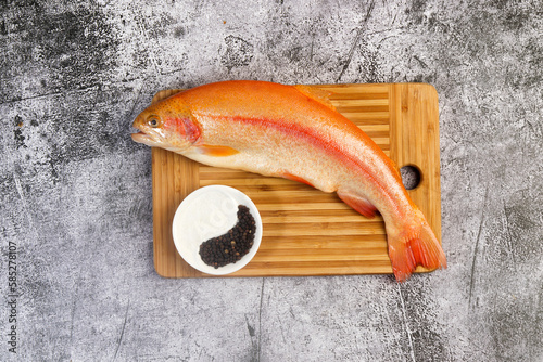Raw amber trout on a cutting wooden board on a dark grey background. Top view, flat lay