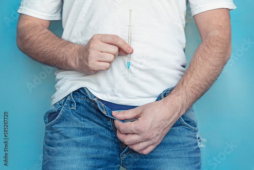 protection of sexually transmitted infections. a man holds a syringe in his hands and takes off his jeans. The concept of treatment of sexually transmitted diseases. photo