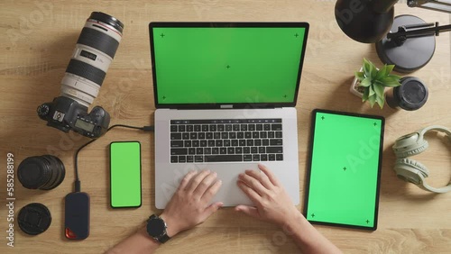 Top View Zoom Out Shot Of A Male Video Editor Using Green Screen Laptop With Green Screen Smartphone And Tablet Next To The Camera In The Workspace At Home
