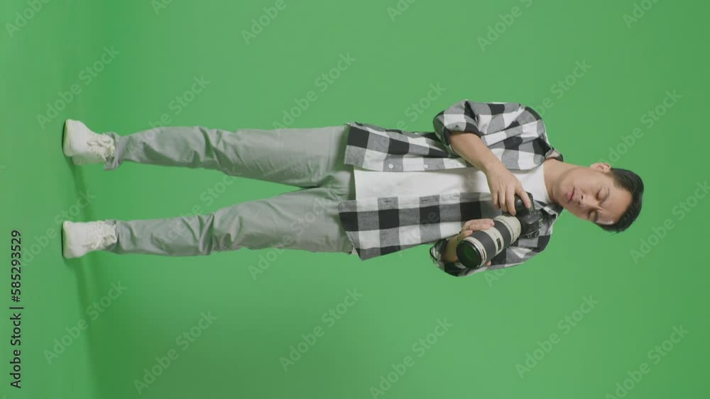 Full Body Of Asian Photographer Looking At The Pictures In The Camera Then Having A Headache While Standing On Green Screen Background In The Studio
