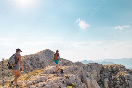 two girls with backpacks walk along a mountain path. © zhukovvvlad