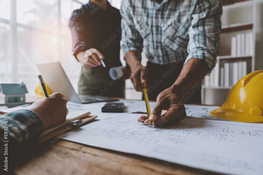A group of engineers and architects are brainstorming, analyzing and taking notes using tape measure to measure house plans. Draft the house structure to establish the correct standards. A group of engineers and architects are brainstorming, analyzing and taking notes using tape measure to measure house plans. Draft the house structure to establish the correct standards.
