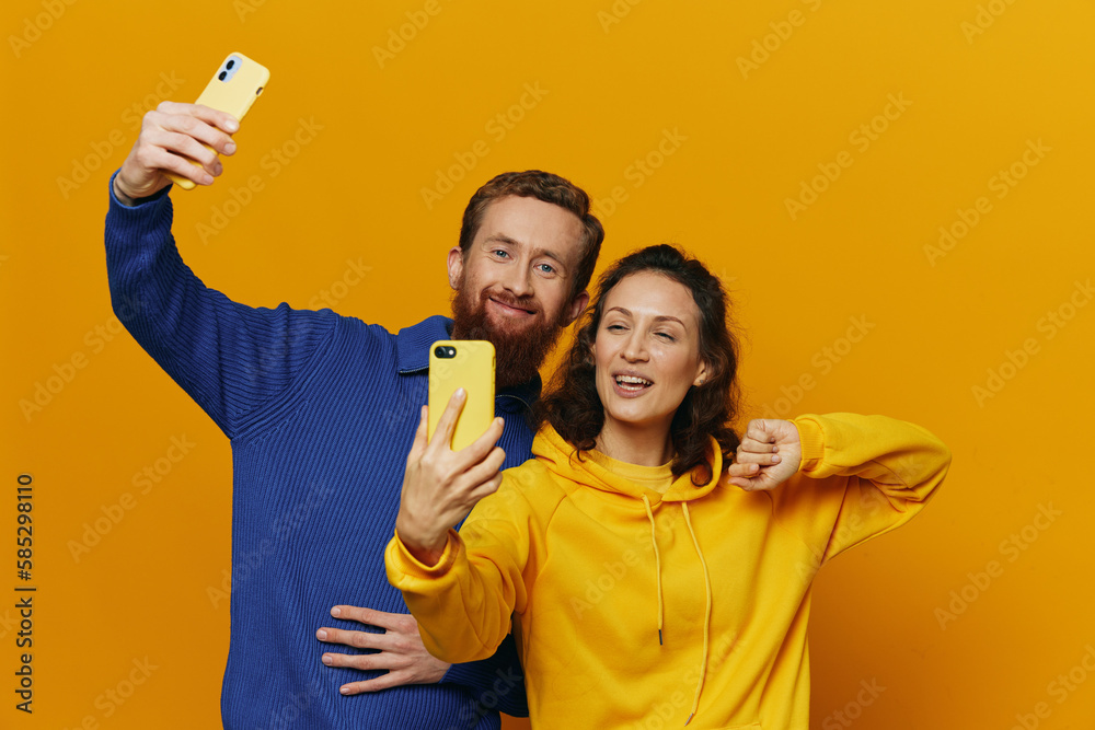 Man and woman couple smiling merrily with phone in hand social media viewing photos and videos, on yellow background, symbols signs and hand gestures, family freelancers. Man and woman couple smiling merrily with phone in hand social media viewing photos and videos, on yellow background, symbols signs and hand gestures, family freelancers.